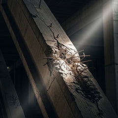 A cracked concrete beam with exposed rebar, illuminated by a dramatic slice of light in a dark space.