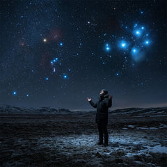 A person stands in a frozen landscape at night, looking up at the constellations of Orion and Pleiades in a star-filled sky.