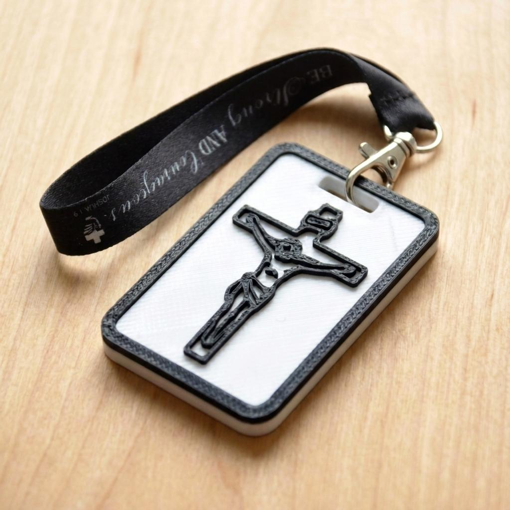 A 3D-printed Eben Tag in Black featuring a raised crucifix design. This NFC-enabled spiritual touchpoint includes a black border and is attached to a fabric lanyard printed with scripture, designed to trigger the Daily Eb devotional.