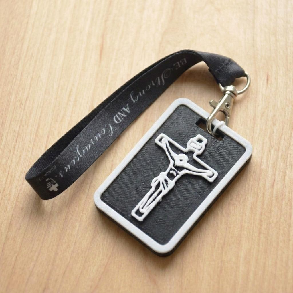 A 3D-printed Eben Tag in Black featuring a raised crucifix design. This NFC-enabled spiritual touchpoint includes a white border and is attached to a fabric lanyard printed with scripture, designed to trigger the Daily Eb devotional.