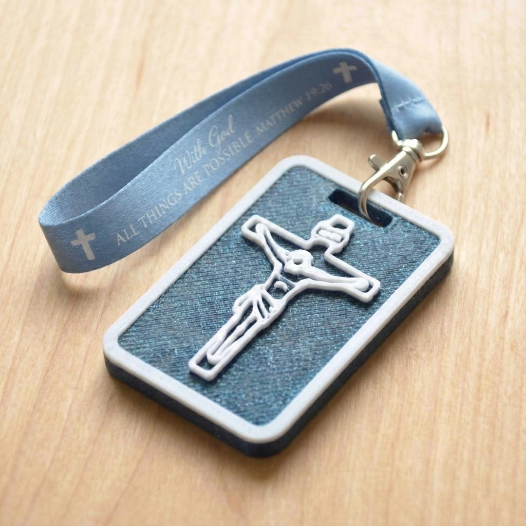 A 3D-printed Eben Tag in Metallic Blue featuring a raised crucifix design. This NFC-enabled spiritual touchpoint includes a white border and is attached to a fabric lanyard printed with scripture, designed to trigger the Daily Eb devotional.