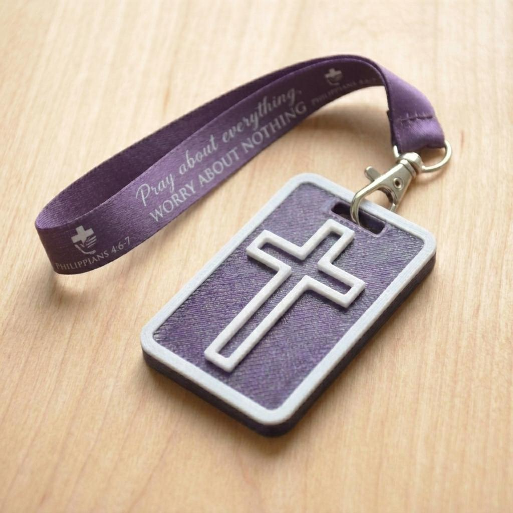 A 3D-printed Eben Tag in Metallic Purple featuring a raised cross design. This NFC-enabled spiritual touchpoint includes a white border and is attached to a fabric lanyard printed with scripture, designed to trigger the Daily Eb devotional.
