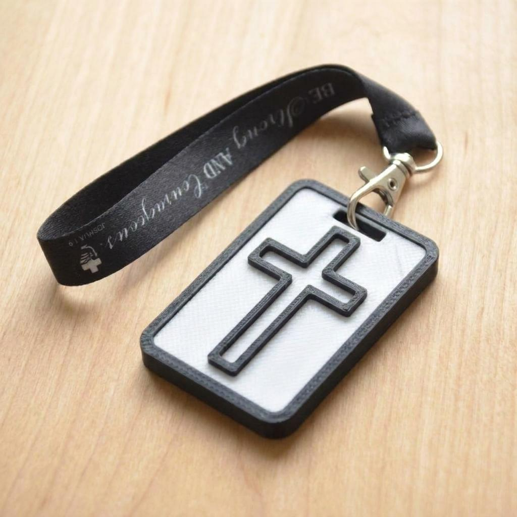 A 3D-printed Eben Tag in White and Black featuring a raised cross design. This NFC-enabled spiritual touchpoint includes a black border and is attached to a fabric lanyard printed with scripture, designed to trigger the Daily Eb devotional.