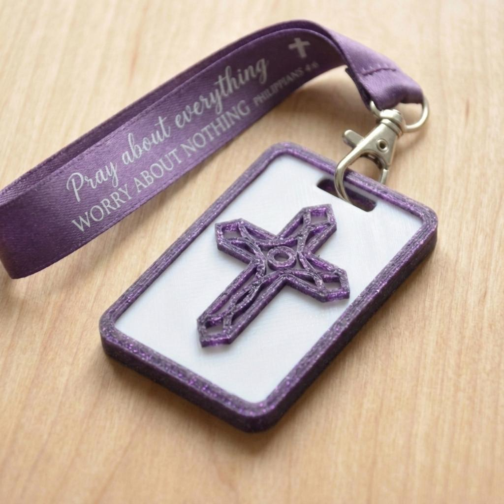 A 3D-printed Eben Tag in White and Purple featuring a raised ornate cross design. This NFC-enabled spiritual touchpoint includes a purple border and is attached to a fabric lanyard printed with scripture, designed to trigger the Daily Eb devotional.